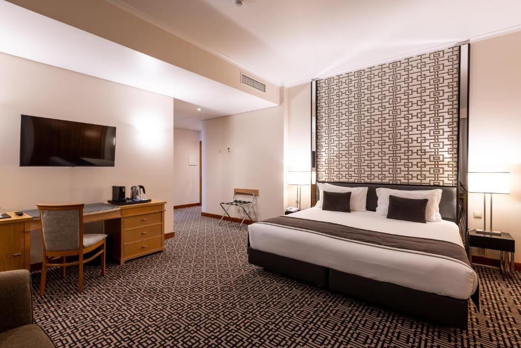 ein Hotelzimmer mit einem großen Bett und einem Schreibtisch in der Unterkunft Hotel Mundial in Lissabon