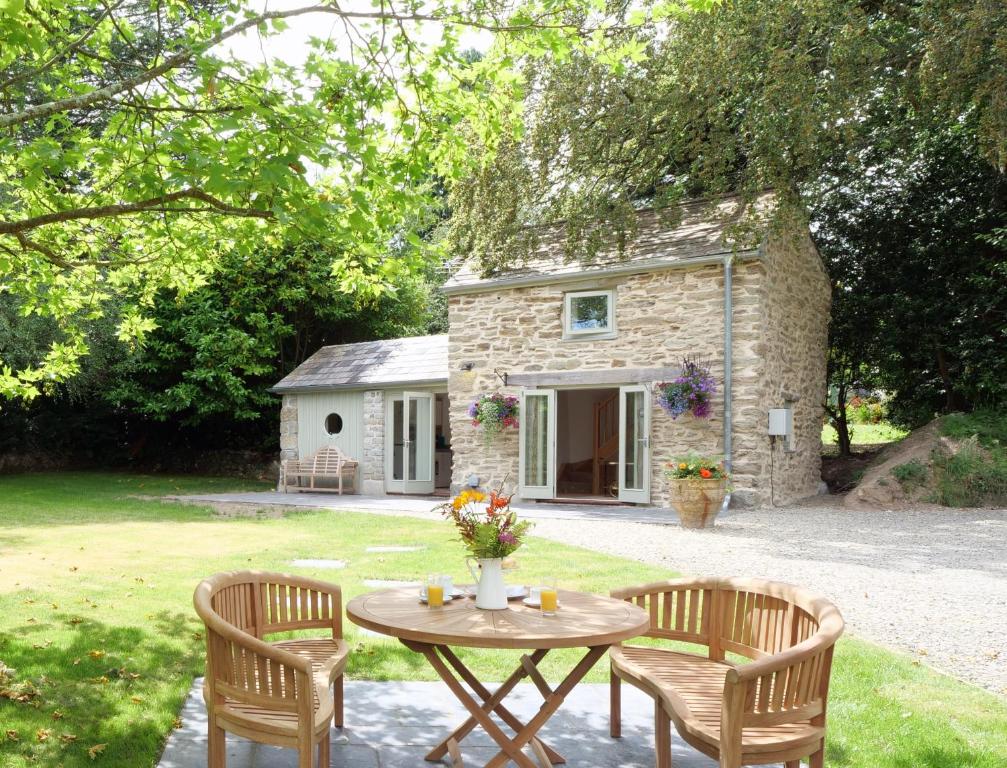 - une table et des chaises devant un cottage en pierre dans l'établissement Pinetum Garden Cottages, à St Austell