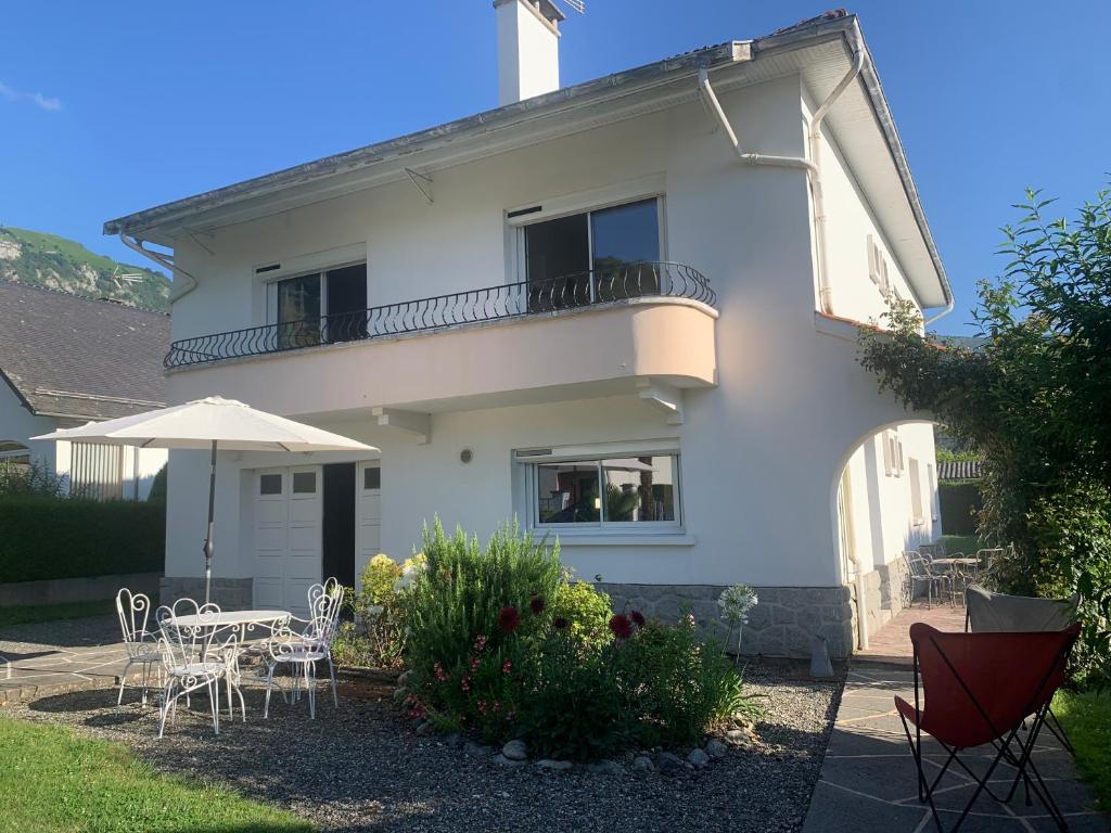 a white house with tables and chairs and an umbrella at Villa de charme jardin vue sur montagnes rénovation 2026 in Argelès-Gazost