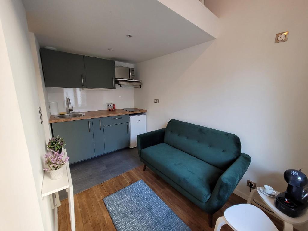 a living room with a green couch and a kitchen at 3D- Studio tout équipé avec cuisine 10 mins de Paris in Issy-les-Moulineaux