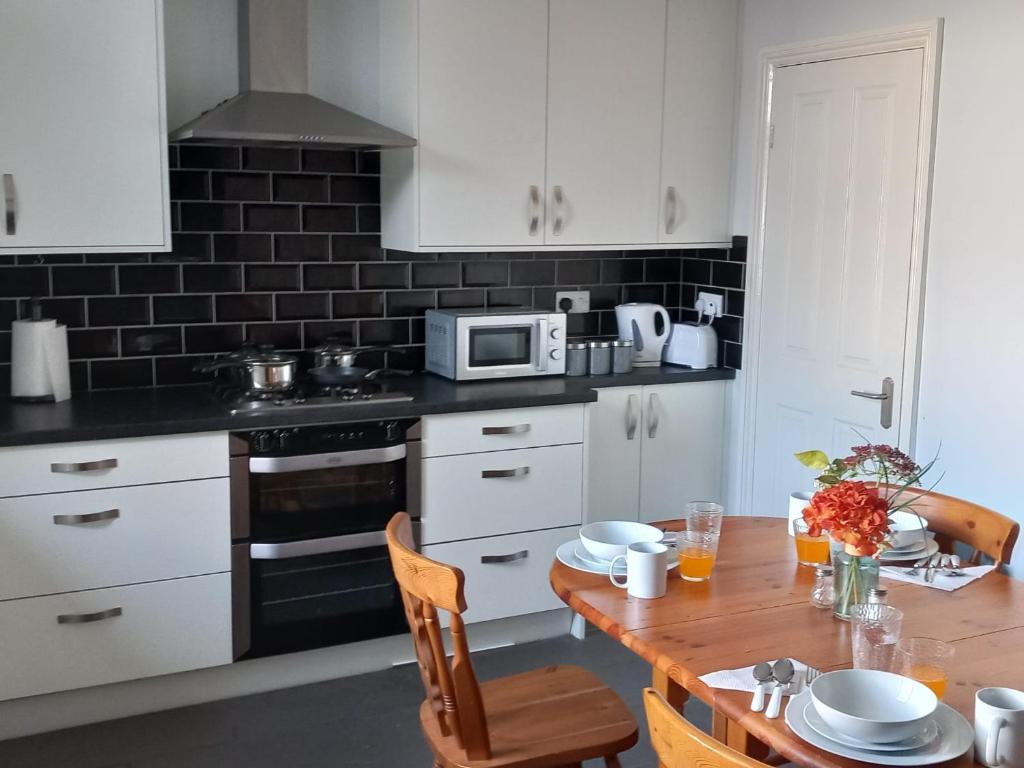 una cucina con armadi bianchi e tavolo in legno di Arise Comfort Home - Dumers Lane, Radcliffe, Bury, Manchester a Radcliffe