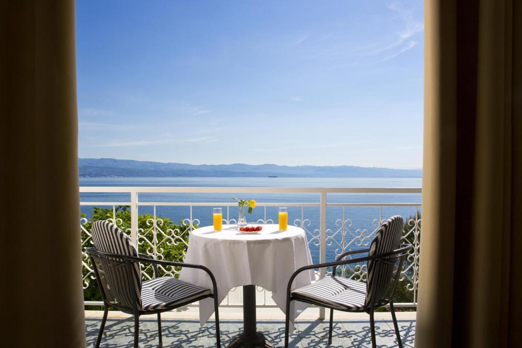 een tafel en stoelen op een balkon met uitzicht op de oceaan bij Hotel Stanger in Lovran