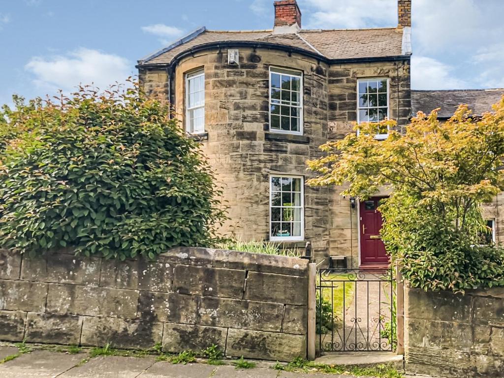 an old stone house with a red door and a fence at Number 1 in Alnwick