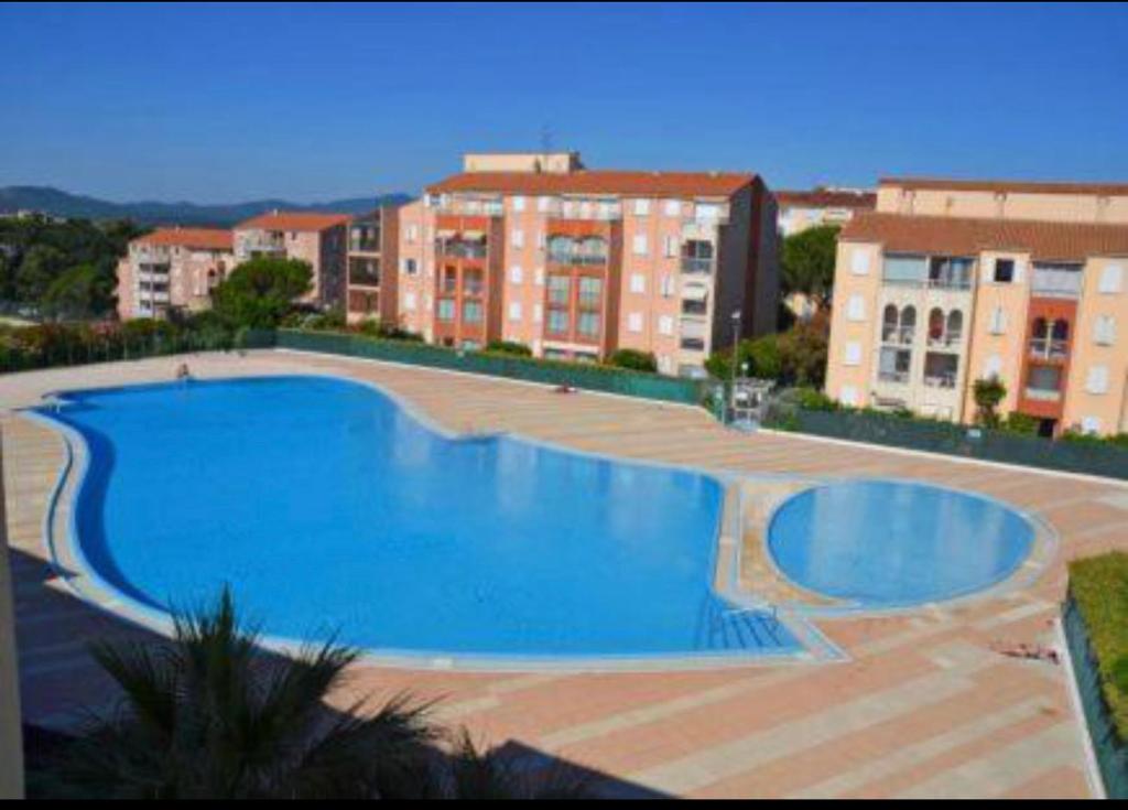 une grande piscine bleue en face de certains bâtiments dans l'établissement Studio dans résidence, piscine lagon, tennis et aire de jeux, à Fréjus