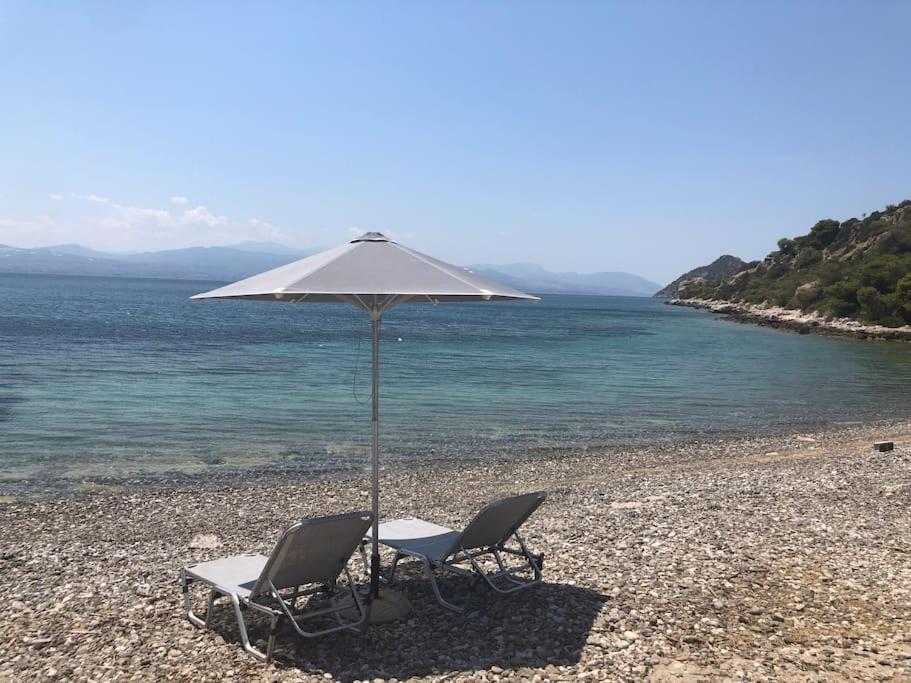 two chairs and an umbrella on a beach at House by the Sea at Skaloma, Loutraki in Vouliagmeni Lake