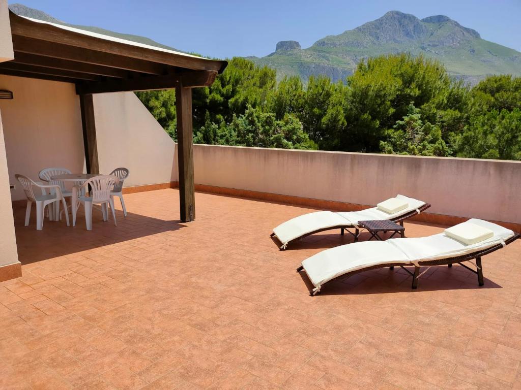 un patio con sedie bianche, tavolo e montagne di La Pineta San Vito Apartment a San Vito lo Capo