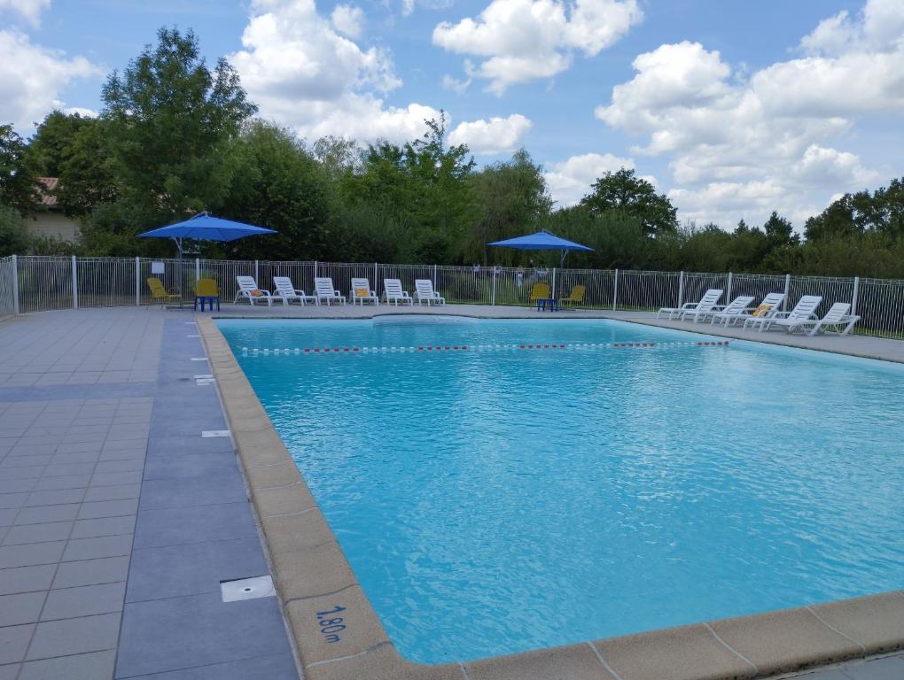 a swimming pool with chairs and blue umbrellas at Pescalis Résidence Les Maisons du Lac in Moncoutant