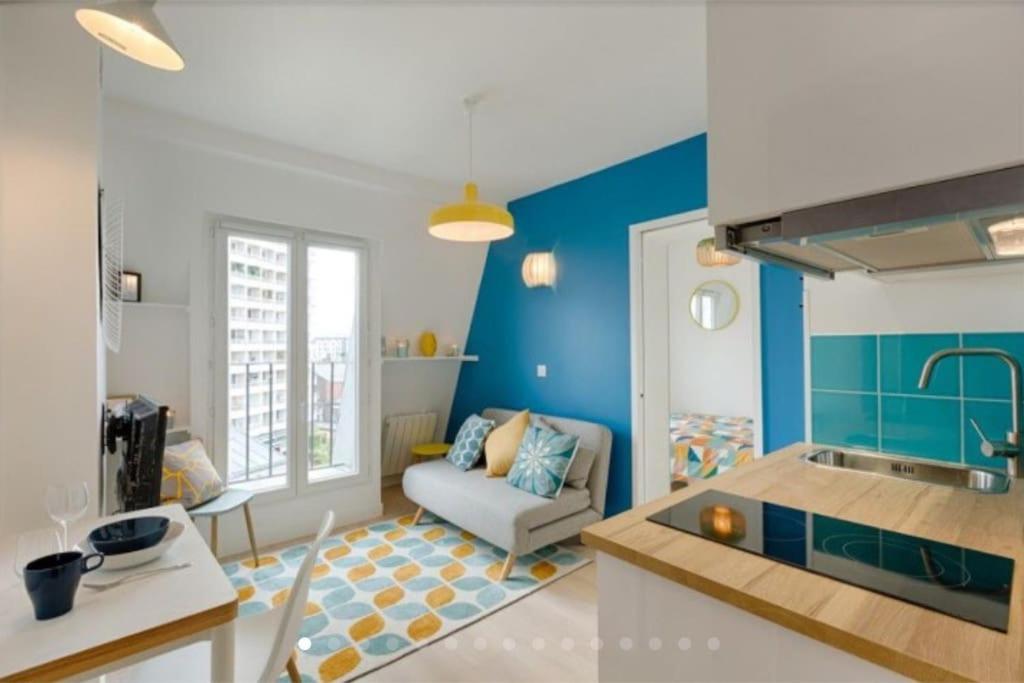 uma cozinha e sala de estar com paredes azuis e um sofá em Charmant 2 pièces calme et cosy em Paris
