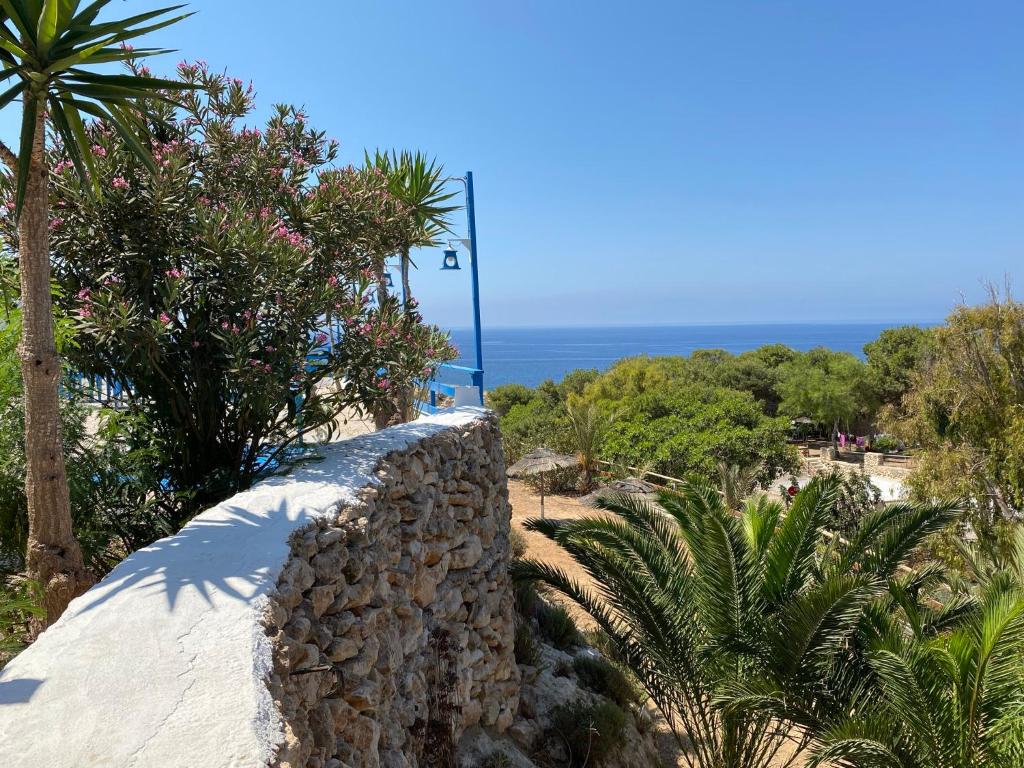 a stone wall with trees and the ocean in the background at Villaggio La Roccia camping in Lampedusa