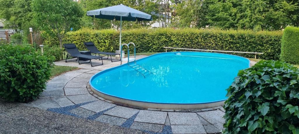a swimming pool with an umbrella and two chairs and an umbrella at Moderne120qm Ferienwohnung in ruhiger Lage Heusweiler - Saarland in Heusweiler