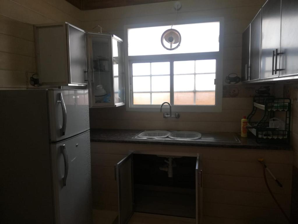 eine Küche mit einer Spüle, einem Kühlschrank und einem Fenster in der Unterkunft APARTMENTS HOQANI in Salalah
