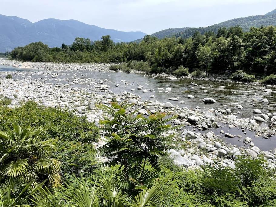 un río con rocas, árboles y montañas en el fondo en Immersi nella natura con accesso al fiume maggia en Locarno