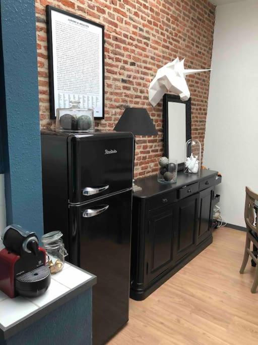 Il dispose d'une cuisine avec un réfrigérateur noir et un mur en briques. dans l'établissement Au cœur du VIEUX-LILLE : Charmant appartement, à Lille