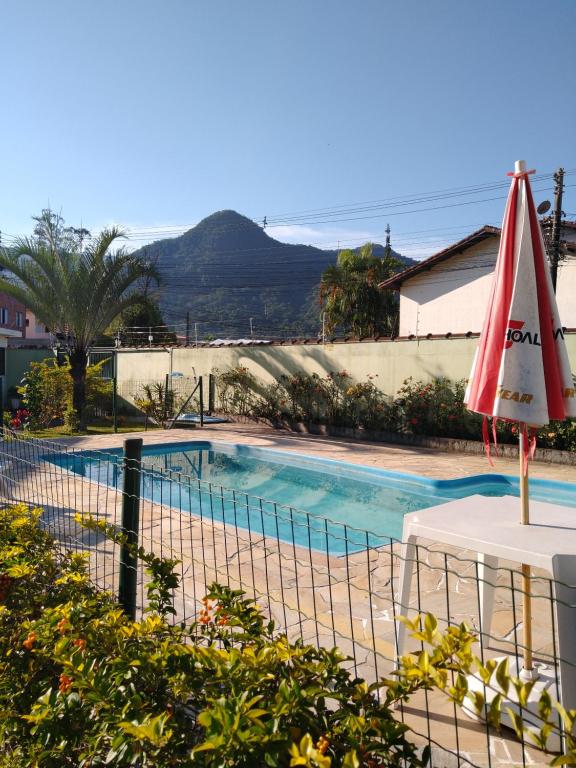 a swimming pool with a red umbrella and a table at Casa Martim de Sá in Caraguatatuba