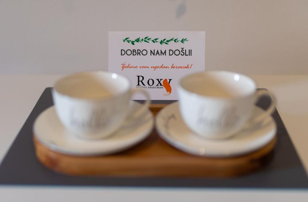 dos tazas y platillos en una bandeja con una tarjeta en Studio Apartman Roxy en Fužine