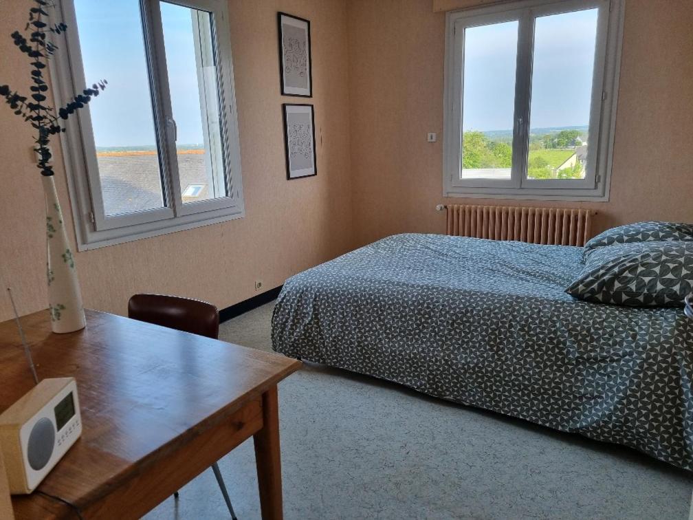 een slaapkamer met een bed, een tafel en 2 ramen bij Chambre dans maison à partager in Talensac