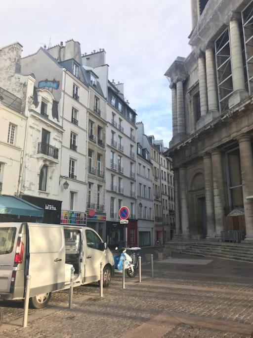 two cars parked on a city street with buildings at Appartement design à la bourse du commerce in Paris
