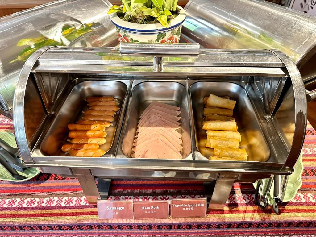 A covered hot-food tray with labeled sausage, ham pork and vegetable spring rolls.