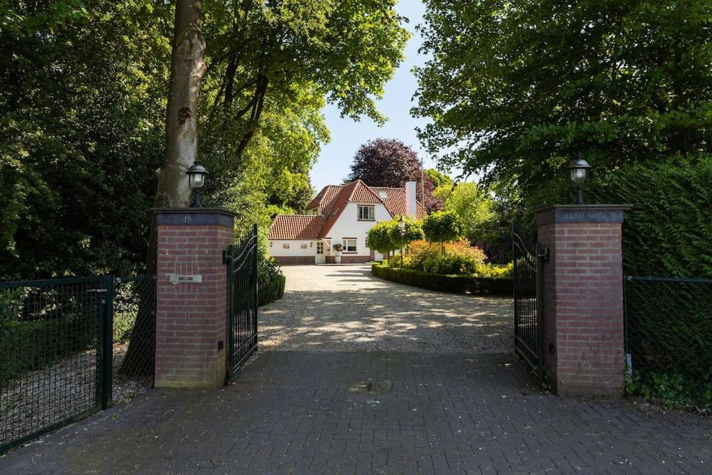 een poort naar een oprit met een huis op de achtergrond bij Stylish villa 12p with private pool in the Veluwe in Garderen