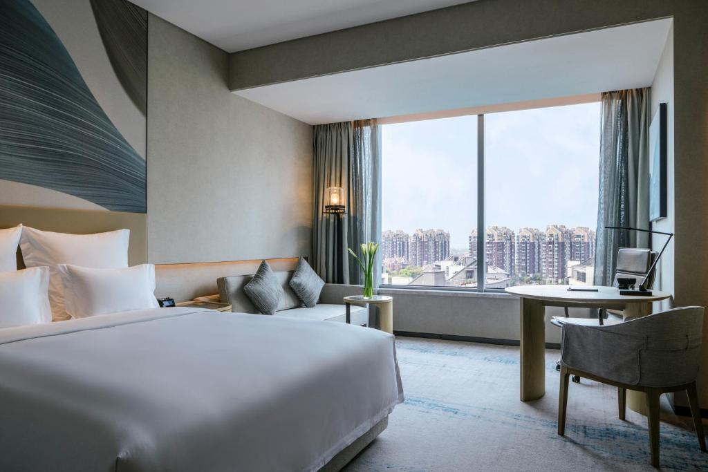 Habitación de hotel con cama, escritorio y ventana grande. en Pullman Shanghai Qingpu Excellence en Shanghái