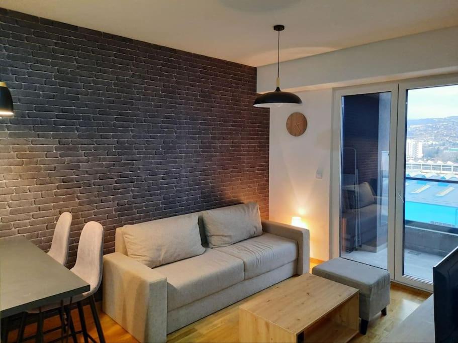 uma sala de estar com um sofá, uma mesa e uma parede de tijolos em Cozy one-bedroom apartment in Skopje em Skopje