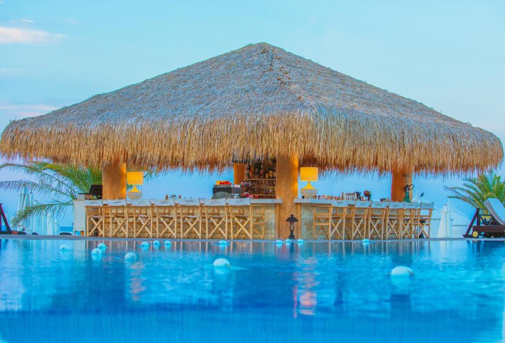 een resort met een rieten dak en een zwembad bij ОАЗИС РИЗОРТ&СПА-премиум апартаменти с гледка море in Lozenets