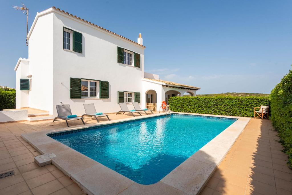 a villa with a swimming pool in front of a house at Villa Cala Llonga in Mahón