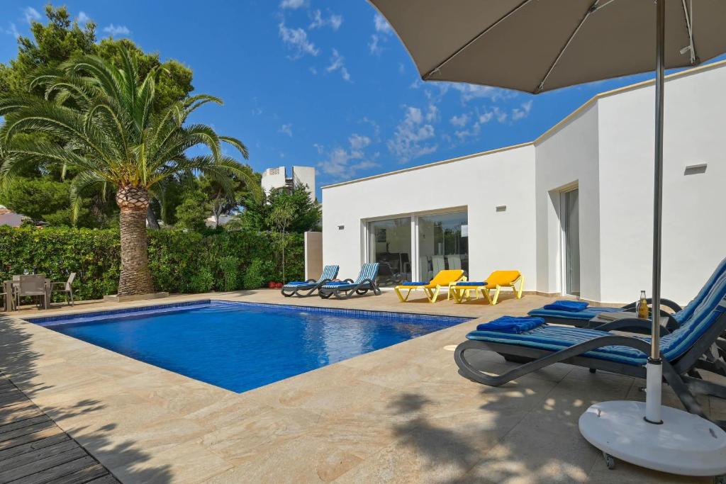 a swimming pool with chairs and an umbrella next to a house at Mercedes in Jávea