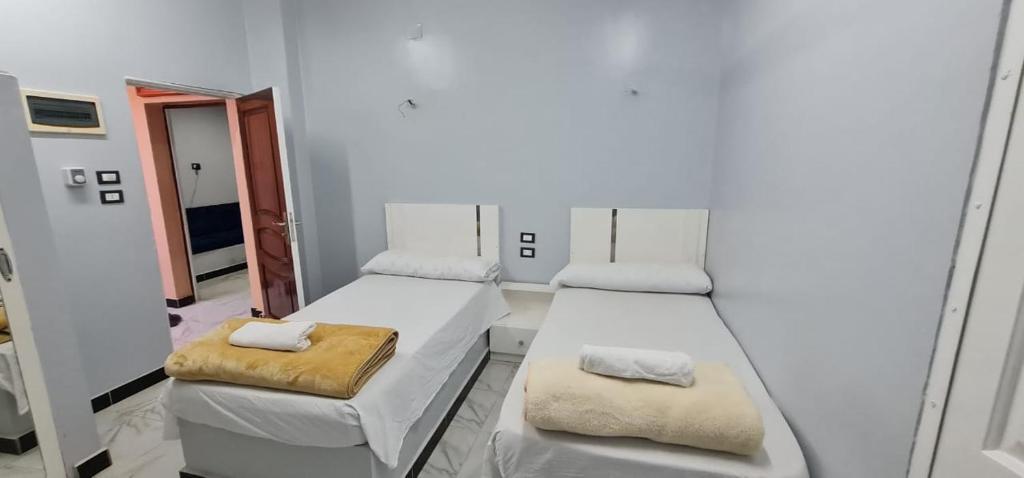 Habitación blanca con 2 camas y espejo. en Hamo Fathy Nubian House, en Asuán