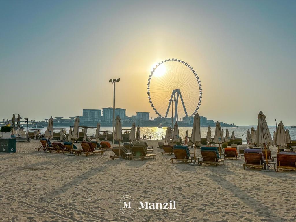 a beach with chairs and a ferris wheel in the background at Manzil - Lavish 3BR in JBR with Sea Views and 5 min walk to beach in Dubai