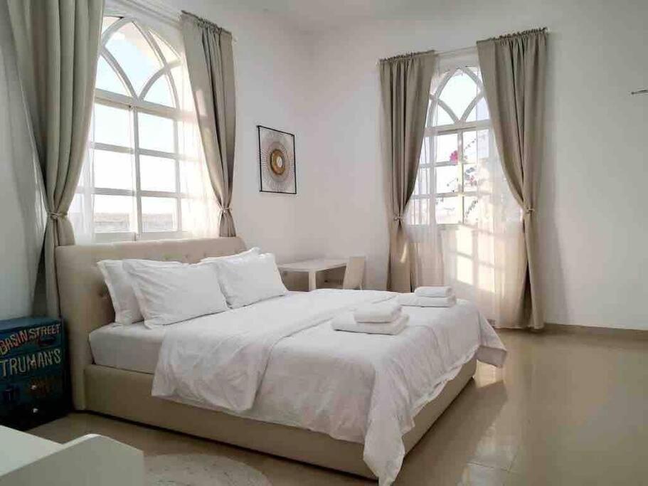 a bedroom with a bed with white sheets and two windows at Villa 9 Palms Beach in Ras al Khaimah