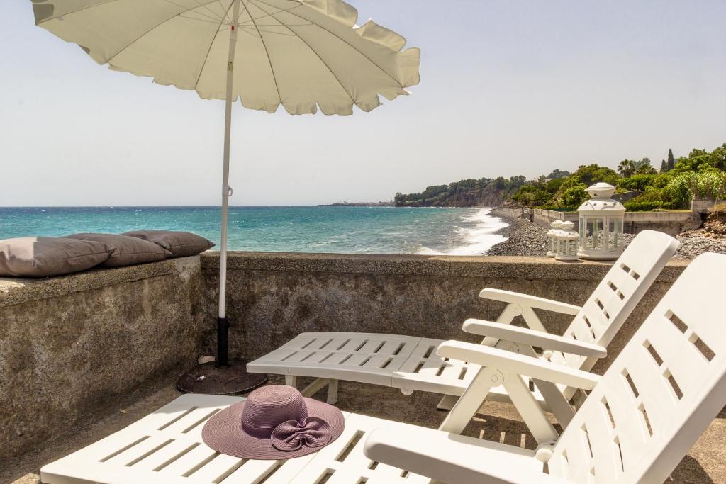 two white chairs and an umbrella next to the ocean at Sea paradise - il mare sotto la finestra in Riposto