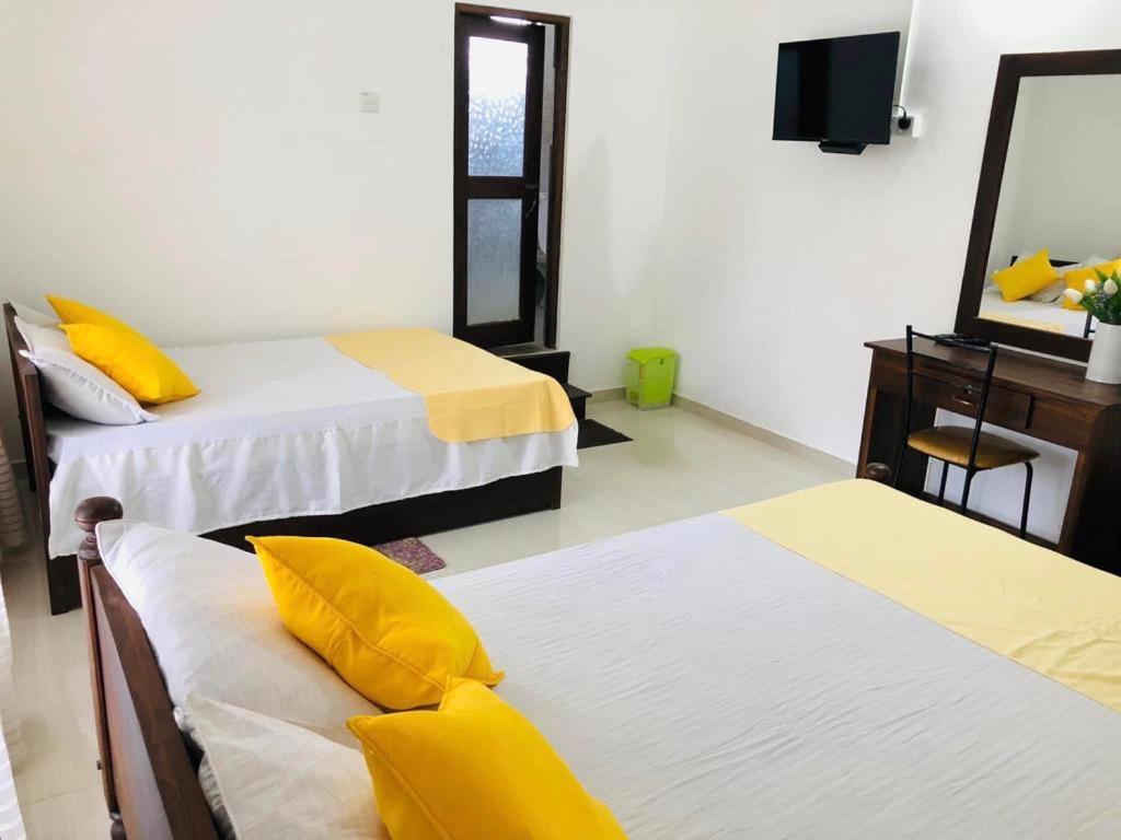 Habitación con 2 camas con almohadas amarillas y espejo. en Castile inn en Puttalam