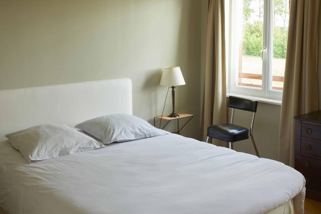 a bedroom with a white bed with a chair and a window at La Maison de Charlotte in Doudeville