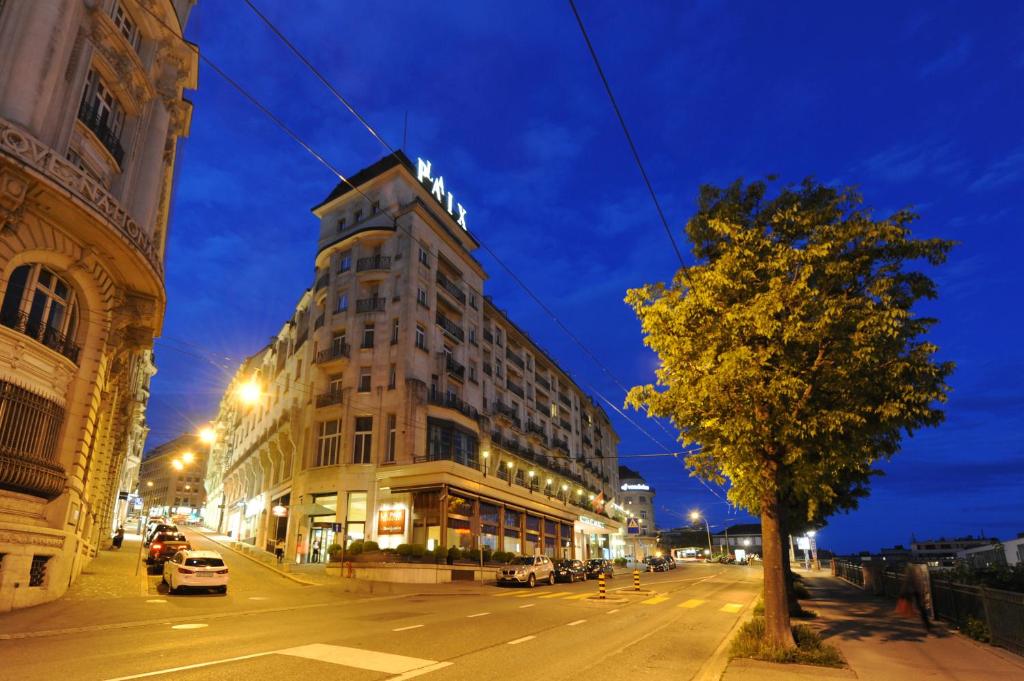 un grand bâtiment sur une rue de la ville la nuit dans l'établissement Hôtel de la Paix Lausanne, à Lausanne