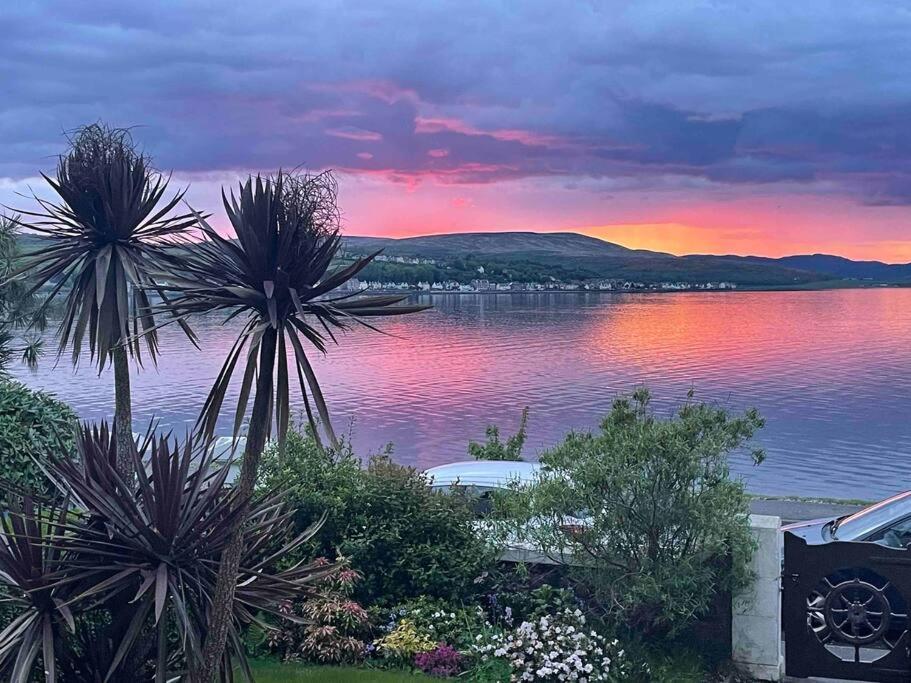 a sunset over a body of water with palm trees at Bayside - Breathtaking views of the Clyde in Rothesay