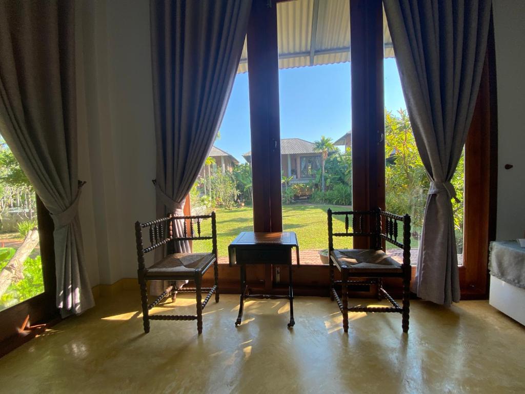 two chairs and a table in a room with large windows at BaanSuk Sukhothai Resort in Sukhothai