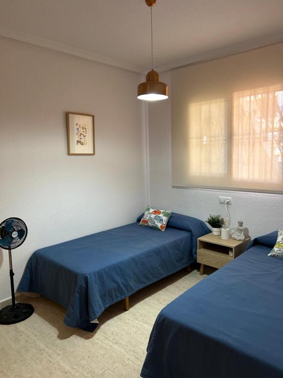 2 Betten in einem Zimmer mit blauer Bettwäsche und einer Lampe in der Unterkunft Acogedor apartamento en la playa vera in Vera