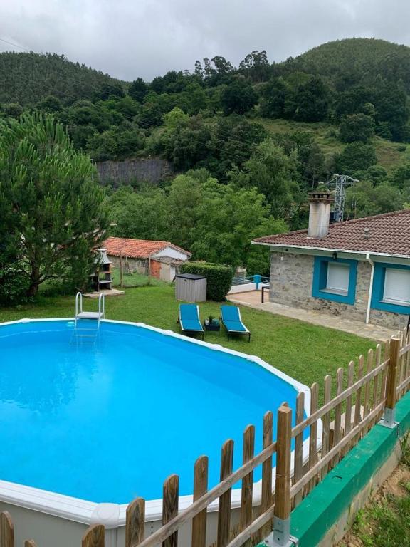 a pool in a yard with two chairs and a house at LA CASA AZUL, un oasis de calma, vistas impresionantes con PISCINA, SALTADOR, BARBACOA y acceso al río Asón in Ramales de la Victoria