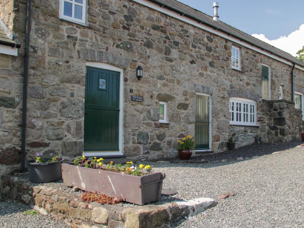 a stone house with a green door and flowers in front at No 2 The Stables in Llangefni