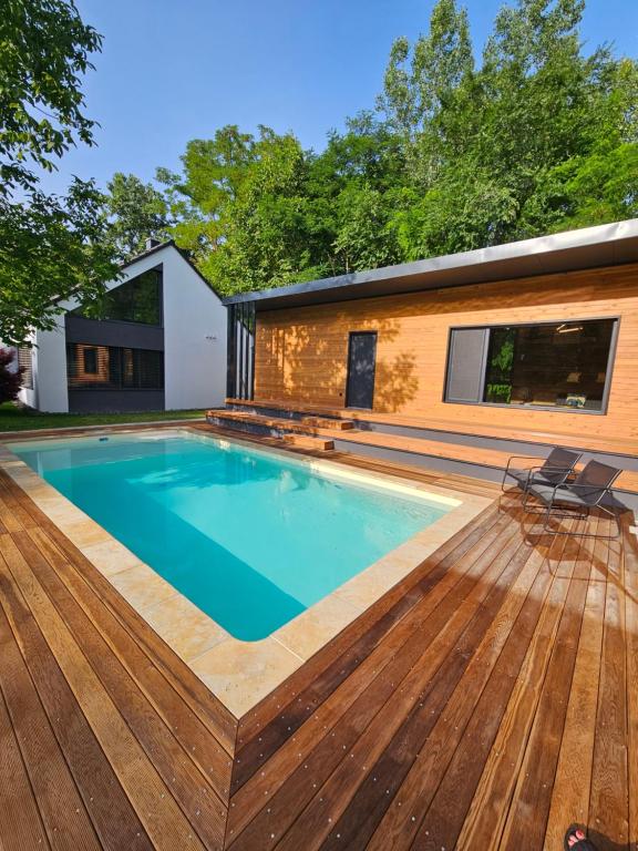 a swimming pool with a wooden deck and a house at Meszes Apartman in Kalocsa