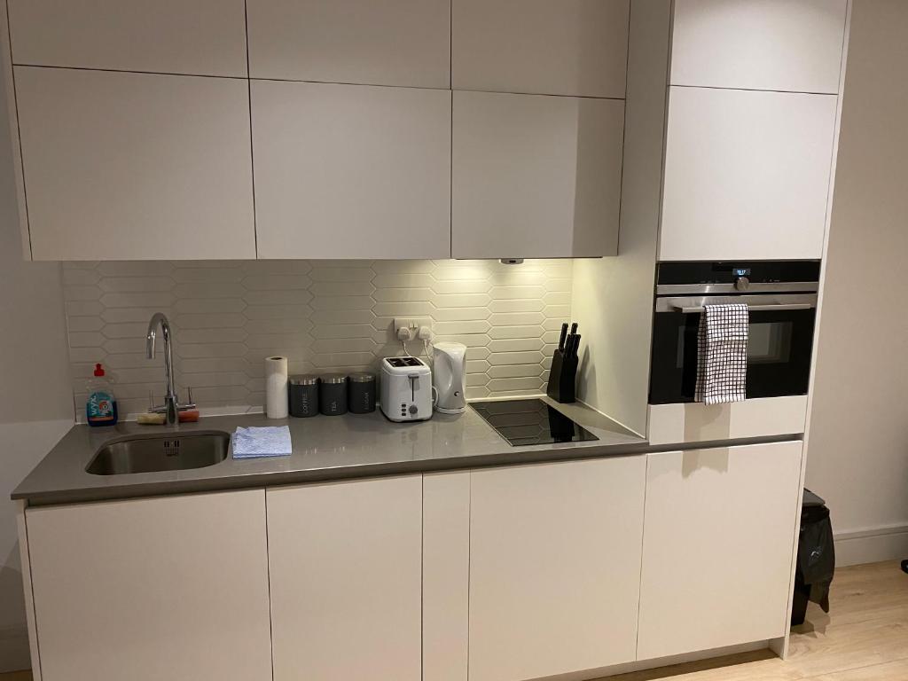 a white kitchen with a sink and a microwave at Nice Apartment Close to Ilford Station , NETFLIX AND WI-FI FREE in Ilford
