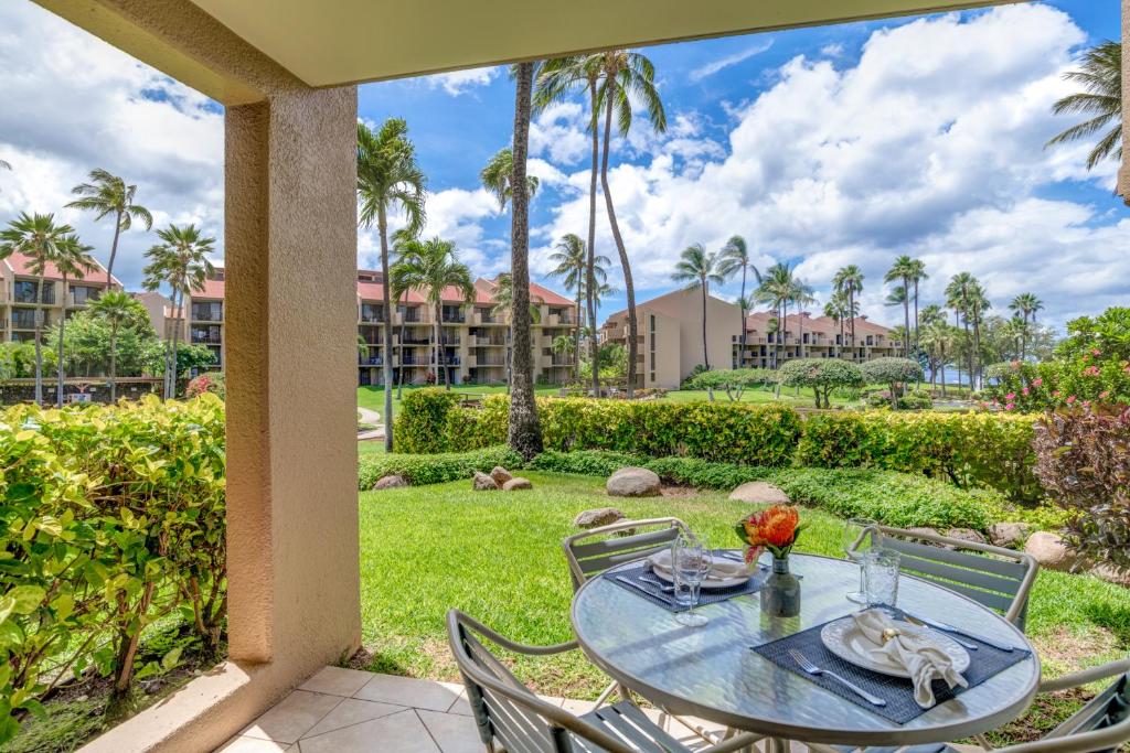 a patio with a table and chairs and palm trees at Kamaole Sands 2-106 in Wailea