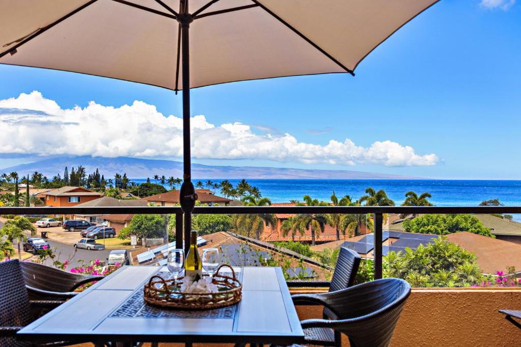 a table with an umbrella on a balcony overlooking the ocean at Kahana Villa E701 in Kahana