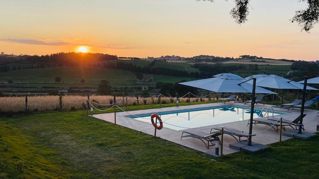 una piscina con ombrelloni e sedie e un tramonto di Agriturismo con cucina Il Favaio a Paciano