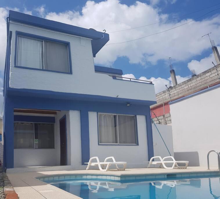 朵索巴的住宿－Amplia casa en Tonsupa con piscina privada y WIFI，蓝色的房子,设有游泳池和两把椅子