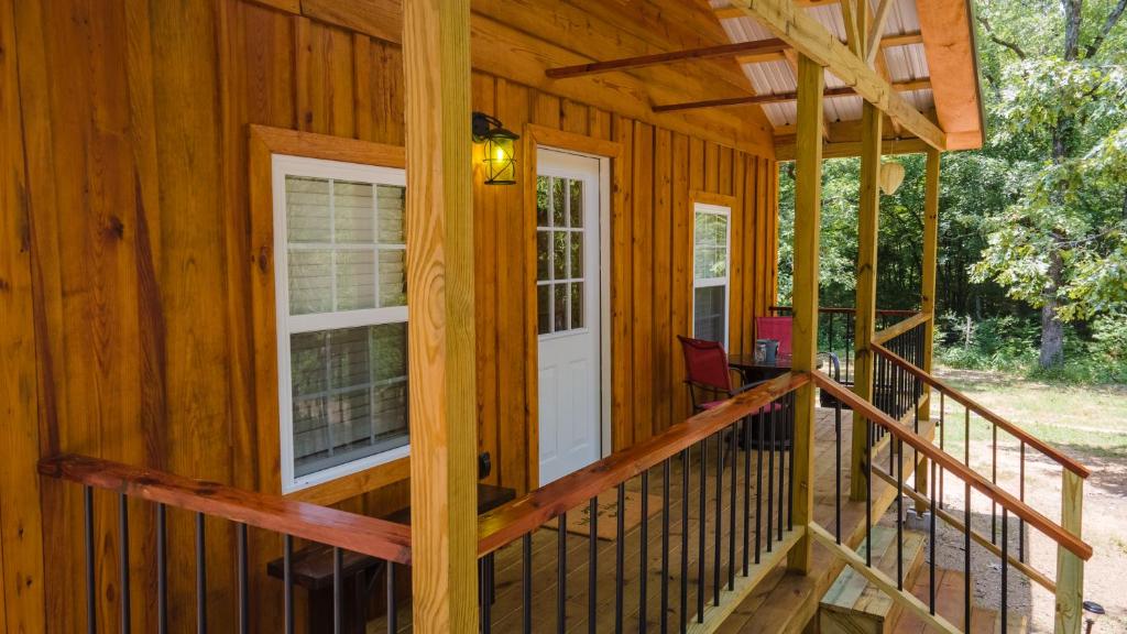 une véranda à l'avant d'une cabane en bois avec une porte blanche dans l'établissement Halfmoon Hideaway-Cozy 2 bdr cabin Mena AR, à Mena