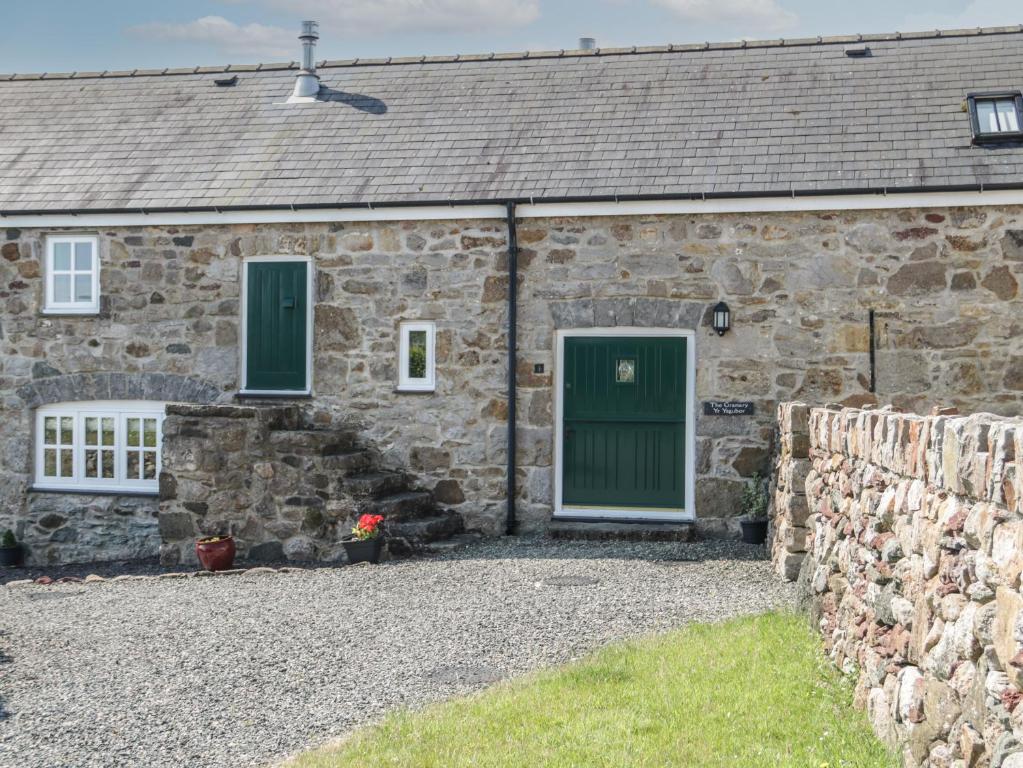 a stone house with green doors and a stone wall at No 1 The Granary in Llangefni