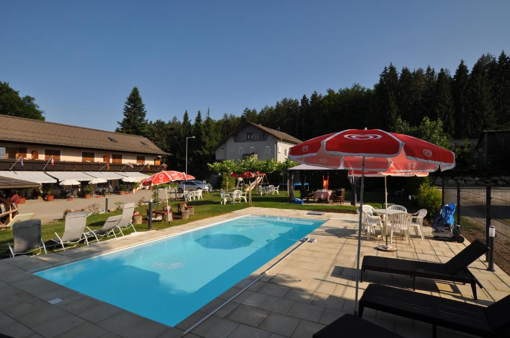 una piscina con sombrilla y sillas rojas, mesa y sombrilla en Kärnten Appartements, en Velden am Wörthersee