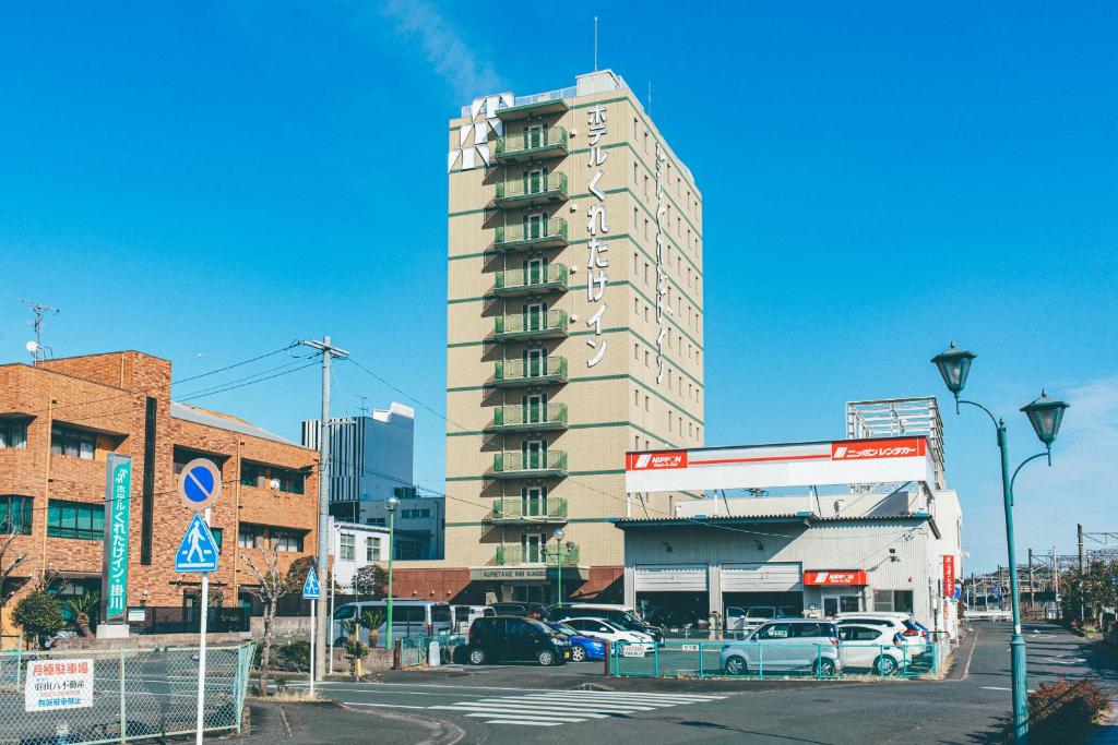 Un edificio alto con coches aparcados en un estacionamiento. en Kuretake-Inn Kakegawa, en Kakegawa